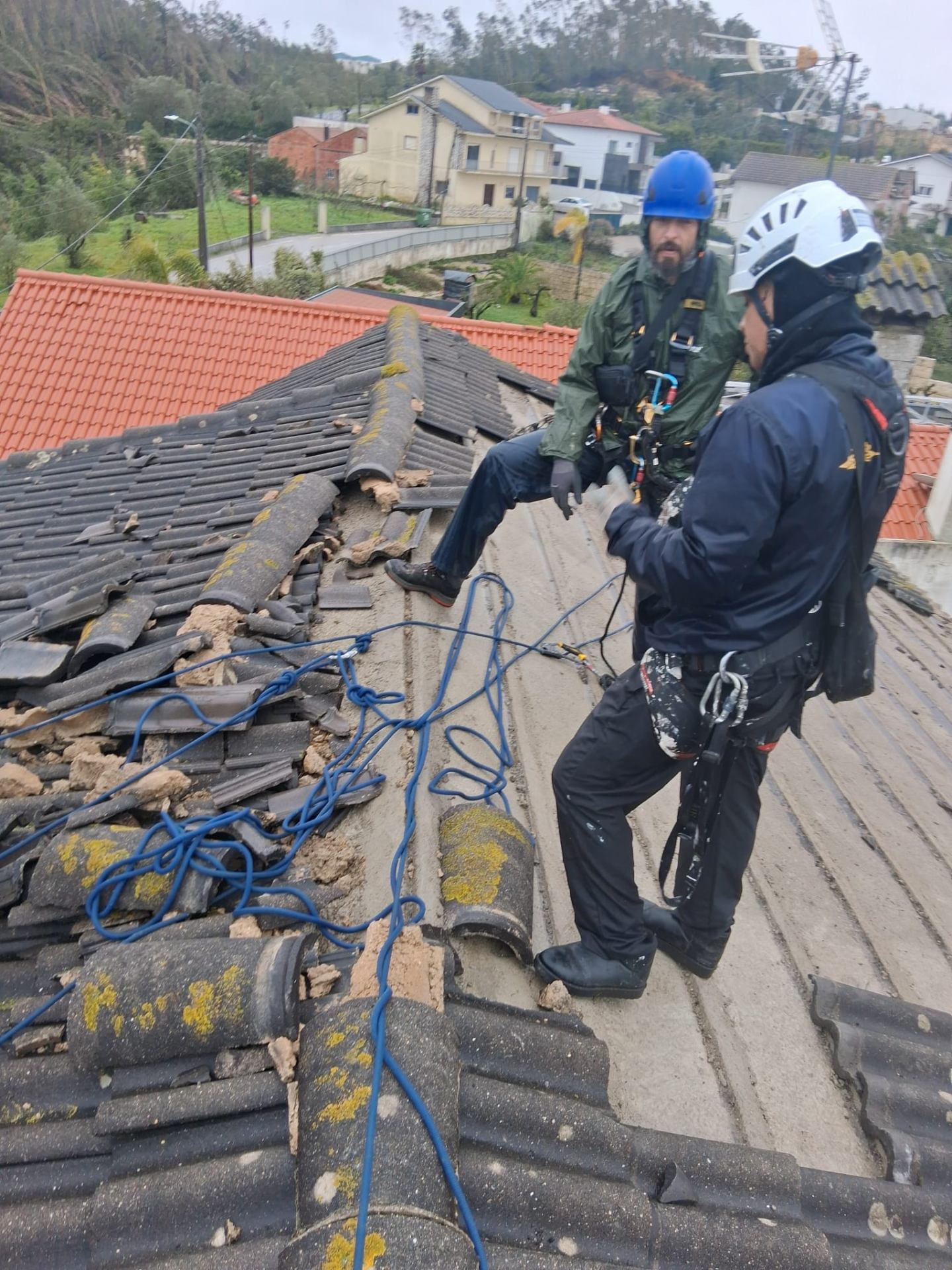 Equipa com arnês a reparar telhado com telhas danificadas