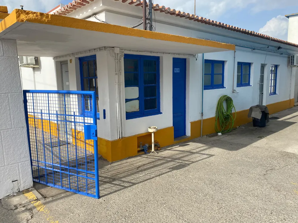Fachada industrial pintada de branco e azul, com portão e rodapés amarelos