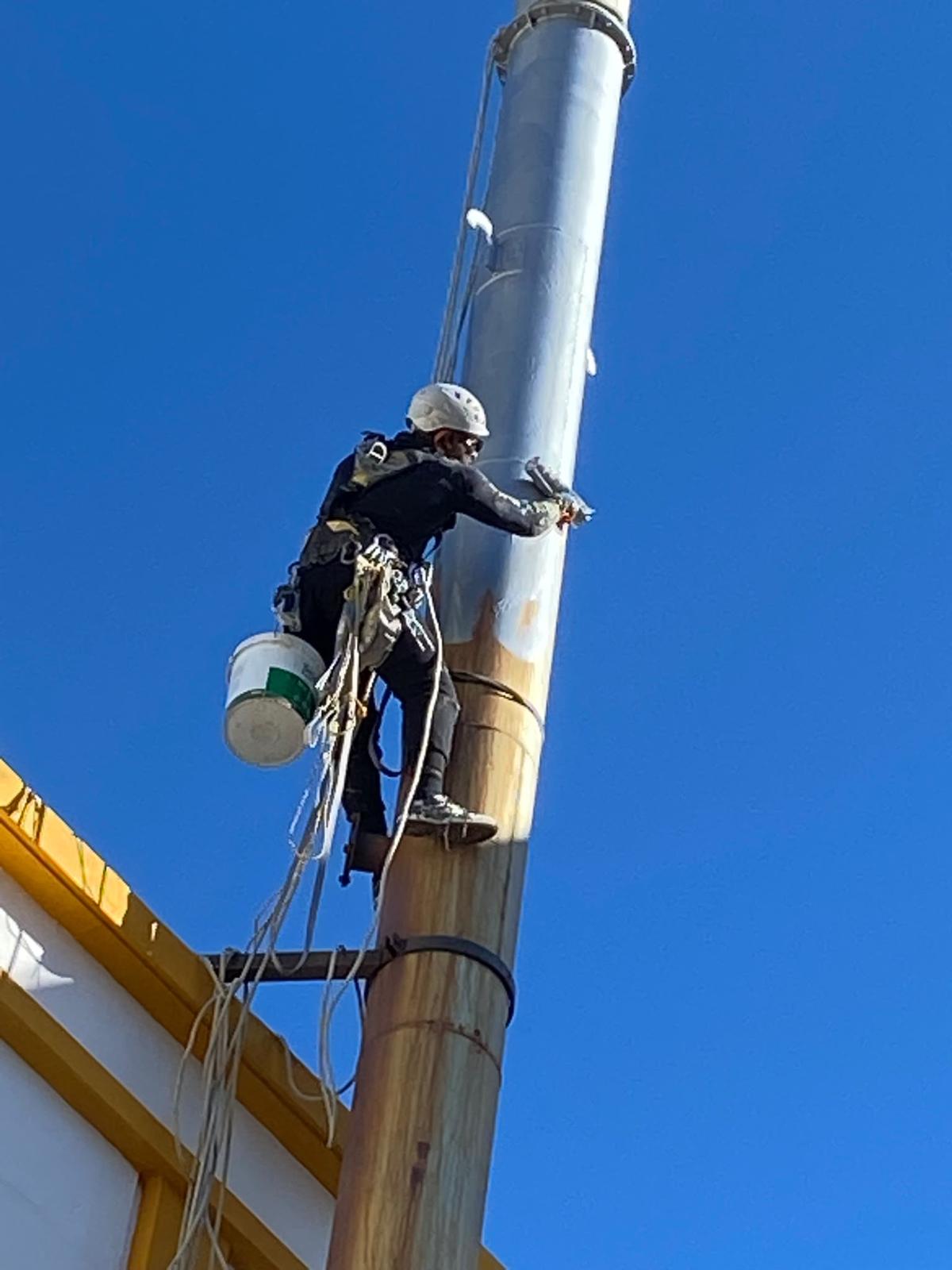 Trabalhador suspenso em rapel a pintar chaminé industrial